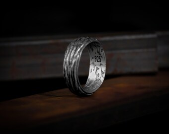 May include: A silver ring with a textured band and a design on the inside of the band. The design includes the number "925" and a floral pattern.