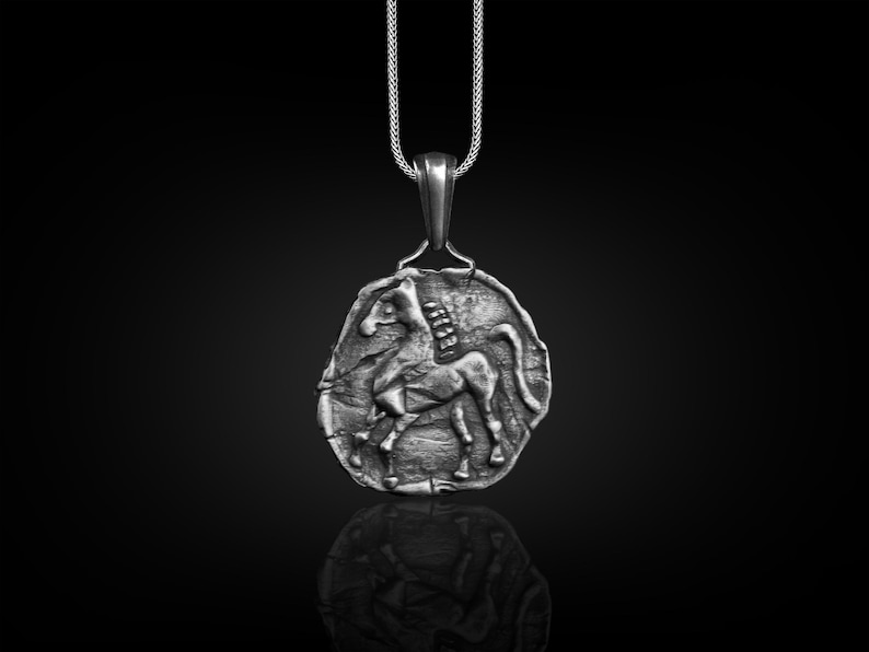 May include: A silver pendant necklace featuring a detailed depiction of a horse in relief. The pendant is round and has a textured surface. The chain is silver and has a delicate design.