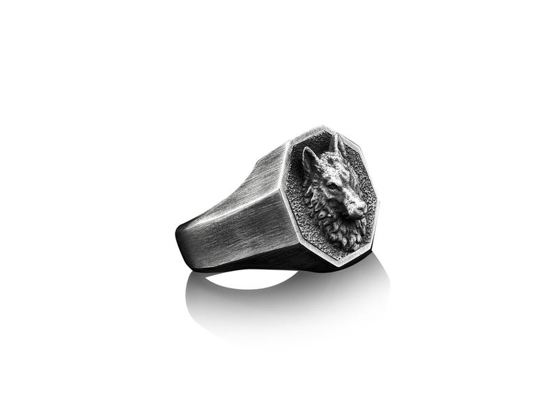 May include: A silver ring with a wolf head design. The ring is octagonal in shape and has a brushed finish.