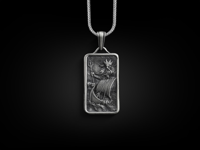 May include: A silver pendant necklace featuring a rectangular charm with a detailed engraving of a mythical sea god holding a trident and riding a ship.