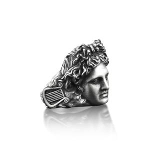 Peut inclure: Une bague en argent avec un buste sculpt&eacute; d&eacute;taill&eacute; d'un homme avec une lyre. Les cheveux de l'homme sont coiff&eacute;s en un design boucl&eacute; et fluide.