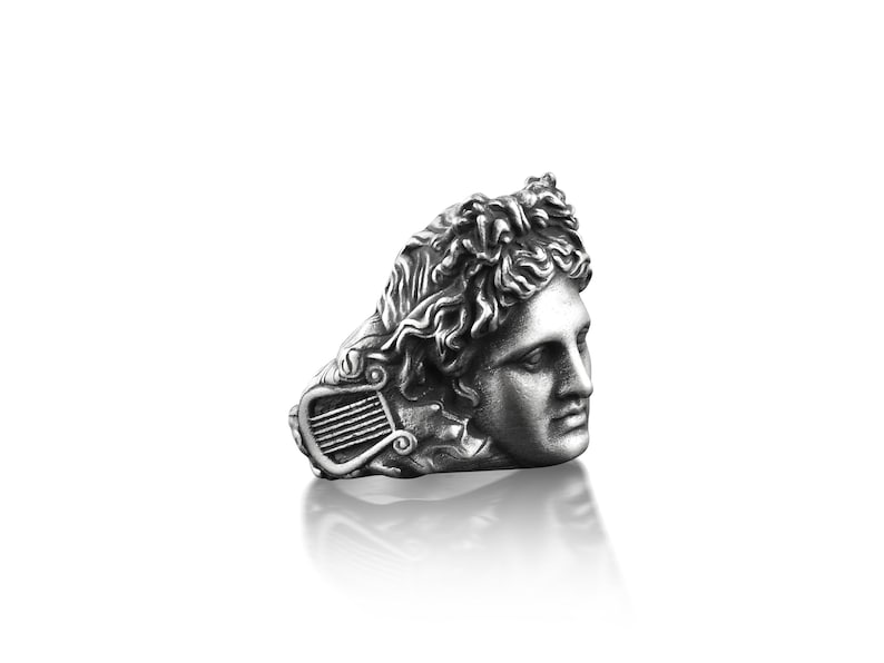Peut inclure: Une bague en argent avec un buste sculpt&eacute; d&eacute;taill&eacute; d'un homme avec une lyre. Les cheveux de l'homme sont coiff&eacute;s en un design boucl&eacute; et fluide.