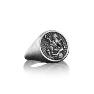 Puede incluir: Un anillo de sello de plata con un dise&ntilde;o detallado de un caballero matando a un drag&oacute;n.