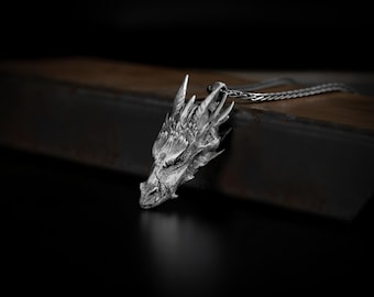 May include: A silver dragon head pendant necklace. The dragon head is detailed and has a textured surface. The necklace is on a chain.