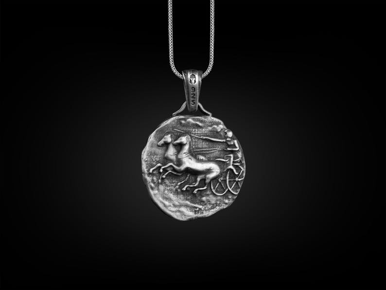 May include: Silver pendant necklace featuring a detailed depiction of a chariot race with two horses and a charioteer. The pendant is round and has a textured surface.