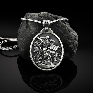 Può includere: Collana con ciondolo in argento raffigurante un santo a cavallo di un leone, che tiene un libro e una penna. Il ciondolo è rotondo e ha una superficie testurizzata.