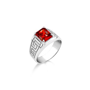 May include: A silver ring with a red square-shaped gemstone and a Greek key design on the band.