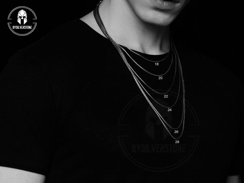 May include: A black and white image of a person wearing a black shirt with a silver chain necklace. The chain is shown in different lengths, with the measurements 18, 20, 22, 24, 26, and 28 inches marked on the image.