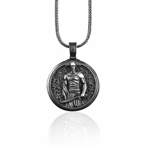 May include: Silver-toned pendant necklace featuring a detailed relief of a warrior in armor, holding a sword. The round pendant is suspended from a matching chain. The warrior is set against a textured background.