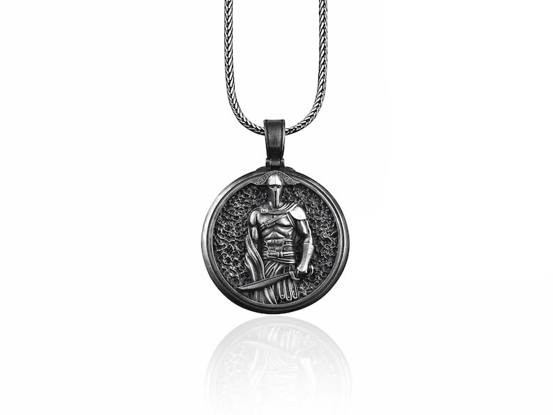 May include: Silver-toned pendant necklace featuring a detailed relief of a warrior in armor, holding a sword. The round pendant is suspended from a matching chain. The warrior is set against a textured background.