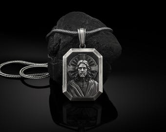May include: A silver pendant necklace with a rectangular pendant featuring a detailed image of Jesus Christ. The pendant is surrounded by a decorative border and a cross.