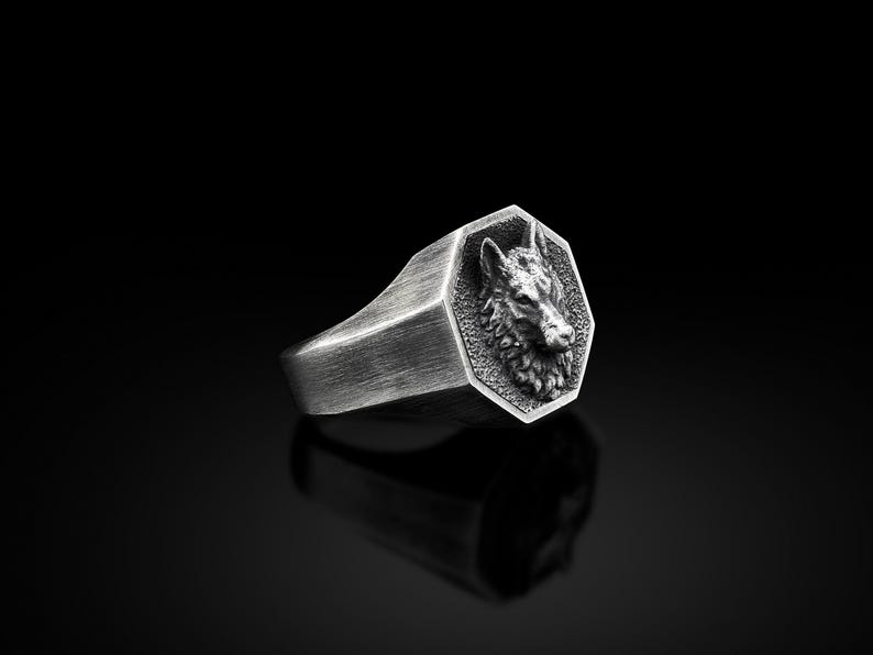May include: A silver ring with a detailed wolf head design on the face of the ring. The ring is octagonal in shape.