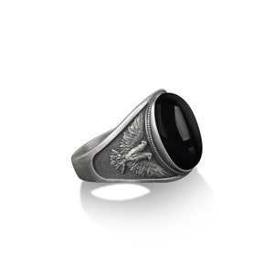May include: A silver ring with a black oval gemstone and an eagle design on the band.