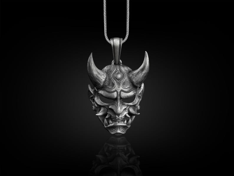 May include: A silver pendant necklace featuring a detailed, three-dimensional Oni mask with horns, a fierce expression, and intricate details.