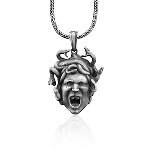 May include: Silver pendant necklace featuring a detailed sculpture of Medusa's head with snakes for hair. The pendant is attached to a silver chain.