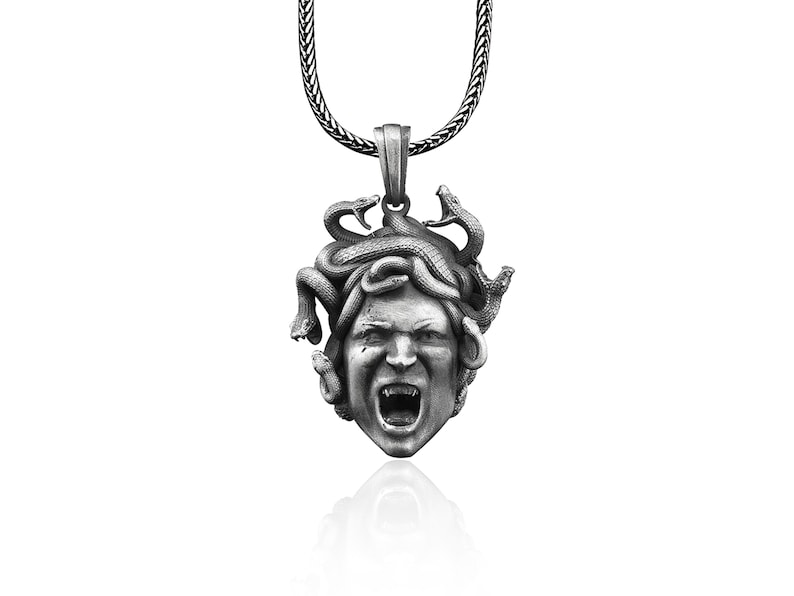 May include: Silver pendant necklace featuring a detailed sculpture of Medusa's head with snakes for hair. The pendant is attached to a silver chain.