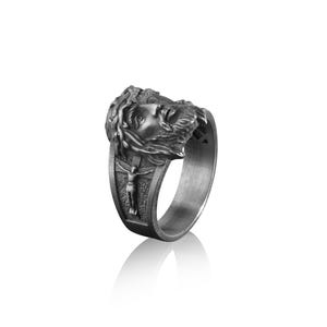 May include: A silver ring with a detailed depiction of Jesus Christ's face and a crown of thorns. The ring also features a smaller image of Jesus on the cross.