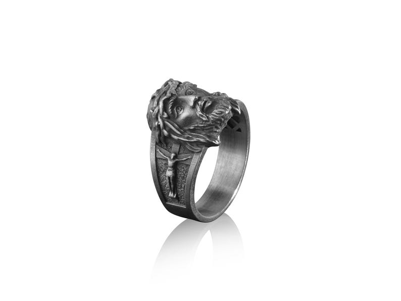 May include: A silver ring with a detailed depiction of Jesus Christ's face and a crown of thorns. The ring also features a smaller image of Jesus on the cross.