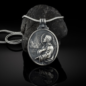May include: Silver pendant necklace featuring a detailed relief of Jesus Christ with a mountain landscape in the background. The pendant is attached to a silver chain.
