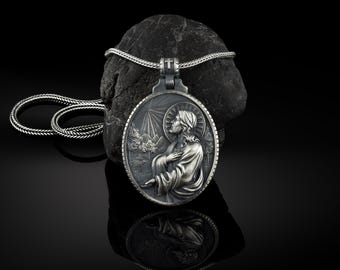 Puede incluir: Collar con colgante de plata que presenta un relieve detallado de Jesucristo con un paisaje de montaña en el fondo. El colgante está unido a una cadena de plata.