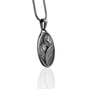 May include: Silver owl pendant necklace with a detailed design of an owl with its wings spread. The pendant is oval shaped and hangs from a silver chain.