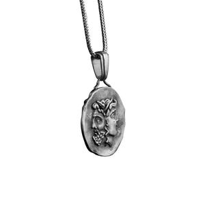 May include: A silver necklace with a round pendant featuring two faces in profile. The pendant is detailed with a textured surface and a chain link design.