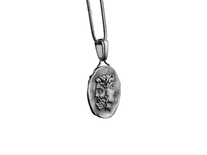 May include: A silver necklace with a round pendant featuring two faces in profile. The pendant is detailed with a textured surface and a chain link design.