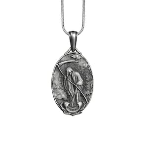 Puede incluir: Un collar con un colgante de plata que presenta una representaci&oacute;n detallada de la Muerte sosteniendo una guada&ntilde;a. El colgante tiene forma ovalada y tiene un aspecto texturizado y envejecido.