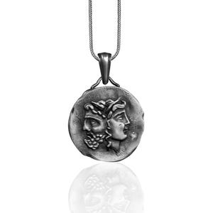 May include: A silver necklace with a round pendant featuring two faces, one with a beard and the other with a crown of leaves.