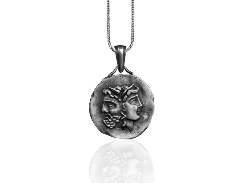 May include: A silver necklace with a round pendant featuring two faces, one with a beard and the other with a crown of leaves.