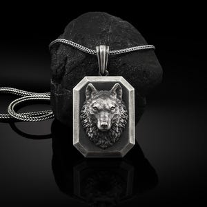 May include: A silver necklace with a wolf head pendant. The pendant is a rectangular shape with a detailed wolf head design.