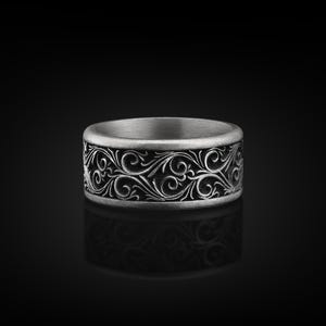 May include: A silver ring with an intricate, engraved design of swirling patterns. The ring is on a black background.