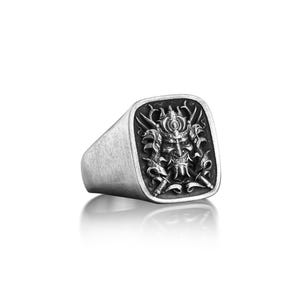 May include: A silver ring with a square face featuring a detailed, black and white engraving of a samurai warrior's mask.