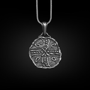 May include: Silver pendant necklace with a round, detailed design featuring a cross and intricate patterns. The pendant is on a silver chain.
