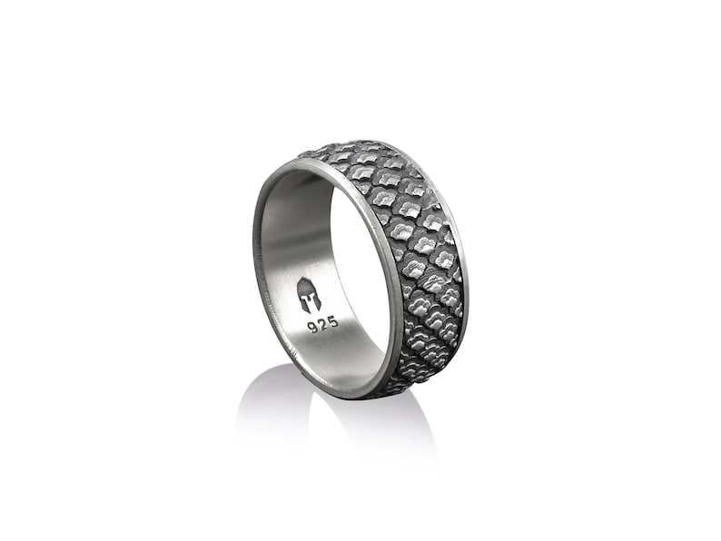 K&ouml;nnte beinhalten: Ein silberner Ring mit einem strukturierten, gemusterten Band. Das Band ist dunkelgrau und hat ein erhabenes Design. Die Innenseite des Rings ist mit "925" und einem kleinen Helm-Symbol gepr&auml;gt.
