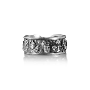 Pu&ograve; includere: Un anello d'argento con un design intricato di fiori e foglie. L'anello &egrave; largo e ha una superficie testurizzata.