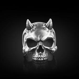 May include: A silver skull ring with horns. The skull is intricately designed with a menacing expression.
