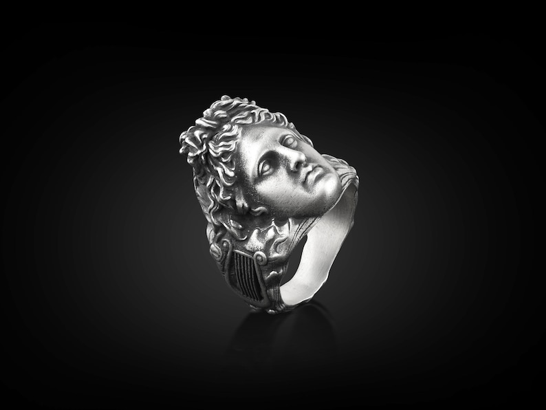 Peut inclure: Une bague en argent avec une sculpture d&eacute;taill&eacute;e d'un visage humain. Le visage regarde vers le haut et vers la droite. La bague est en m&eacute;tal et a une finition lisse.