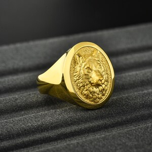 May include: A gold ring with a detailed wolf head design. The ring is oval shaped and has a smooth, polished finish.