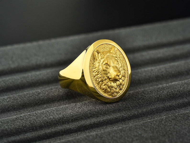 May include: A gold ring with a detailed wolf head design. The ring is oval shaped and has a smooth, polished finish.