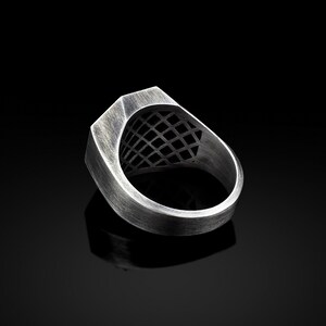 May include: A silver ring with a geometric design on the top. The ring is made of metal and has a brushed finish.
