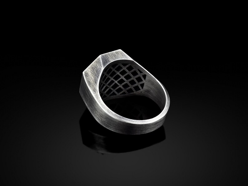 May include: A silver ring with a geometric design on the top. The ring is made of metal and has a brushed finish.