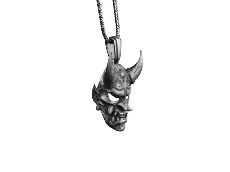 May include: A silver pendant necklace featuring a detailed, stylized oni mask with horns. The mask is a traditional Japanese demon mask.