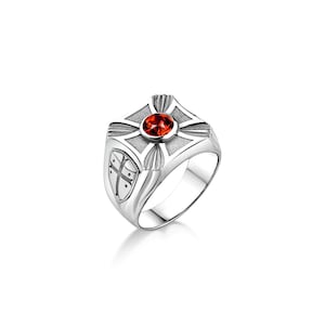 May include: A silver ring with a red gemstone in the centre. The ring features a cross design with a shield on the side.