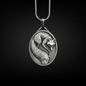 Puede incluir: Collar con colgante plateado con un zorro enrollado en un óvalo. El zorro está finamente detallado. El colgante cuelga de una fina cadena. Una joya elegante.