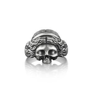 May include: A silver ring with a detailed skull design, featuring a woman's face with long, flowing hair.