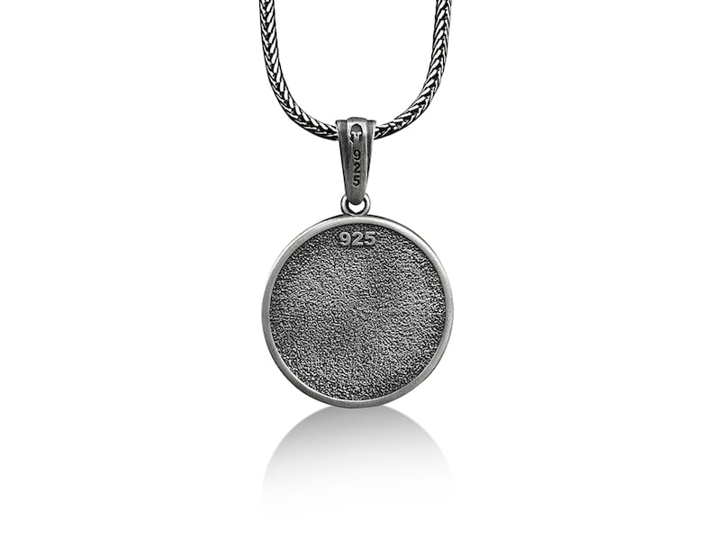 May include: A silver pendant necklace with a textured, circular pendant. The pendant is marked with "925" and hangs from a woven chain. The necklace is displayed against a white background.