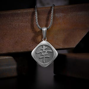 May include: A silver necklace with a square pendant featuring the Japanese kanji character for "happiness" (幸せ). The pendant has a textured, sunburst design.