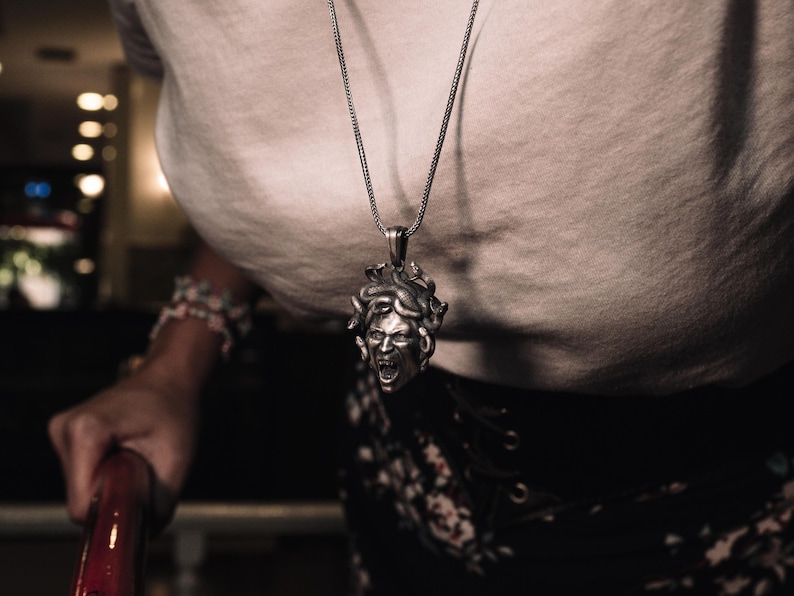 May include: A silver necklace with a detailed pendant of a Medusa head. The pendant is a 3D sculpture with a snarling expression and snakes for hair.