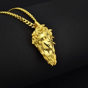 May include: A gold chain necklace with a pendant featuring a detailed, three-dimensional sculpture of a woman's face.